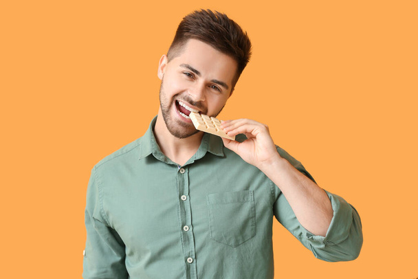 Handsome young man with tasty chocolate on color background - Foto, afbeelding
