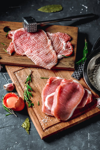 Raw chops and pieces of pork for escalopes on cutting boards with flour, rosemary, bay leaf, sauce on the kitchen table. One piece of meat fell from the chef's hands into flour. Place for text - Foto, Bild