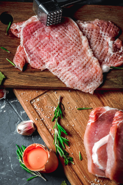 Raw chops and pieces of pork for escalopes on cutting boards with flour, rosemary, bay leaf, sauce on the kitchen table. One piece of meat fell from the chef's hands into flour. Place for text - Foto, imagen