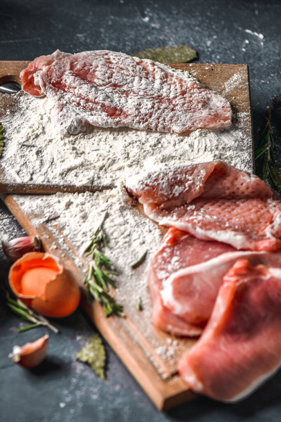 Raw chops and pieces of pork for escalopes on cutting boards with flour, rosemary, bay leaf, sauce on the kitchen table. One piece of meat fell from the chef's hands into flour. Place for text - Foto, Bild