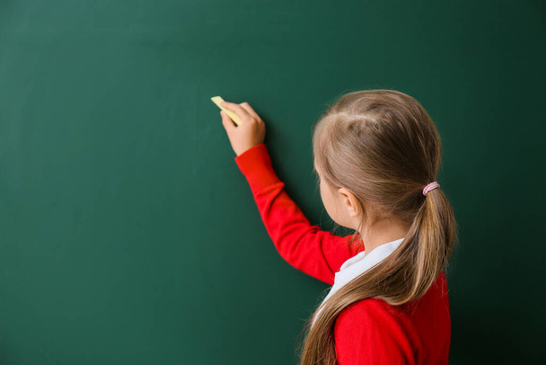Милая маленькая школьница пишет на доске в классе - Фото, изображение