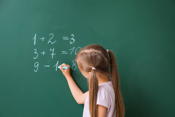 Cute little schoolgirl writing on blackboard in classroom - Photo, image
