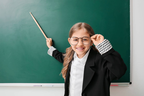 Cute little schoolgirl with pointer near blackboard in classroom - Photo, Image