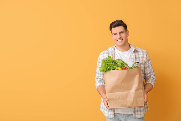 Young man holding bag with food on color background - Фото, зображення