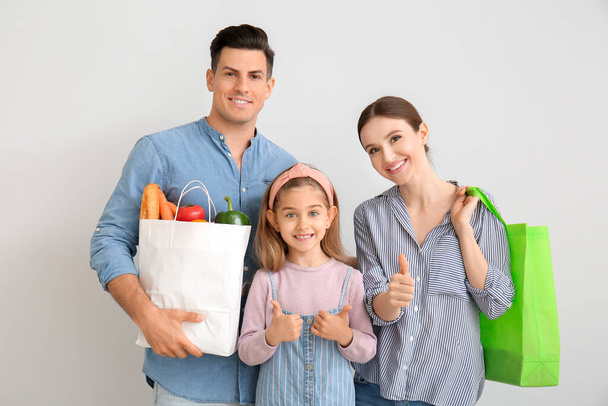 Family with food in bags showing thumb-up gesture on light background - Foto, afbeelding
