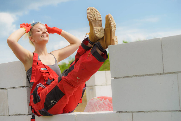 Woman in dungarees relaxing after hard work on construction site. Young female lying outdoor taking a break - 写真・画像