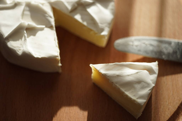 Plátky sýra Camembert a celé s nožem na dřevěné desce. - Fotografie, Obrázek