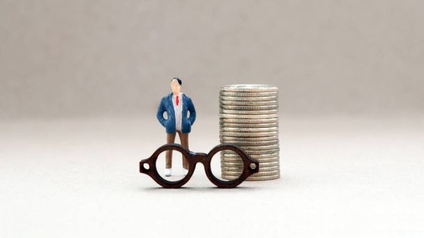Un mucchio di monete e l'uomo in miniatura in piedi dietro gli occhiali
. - Foto, immagini