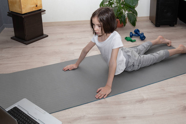 Niño remoto haciendo ejercicios de fitness en casa en su habitación. Niño en pose de serpiente
. - Foto, imagen