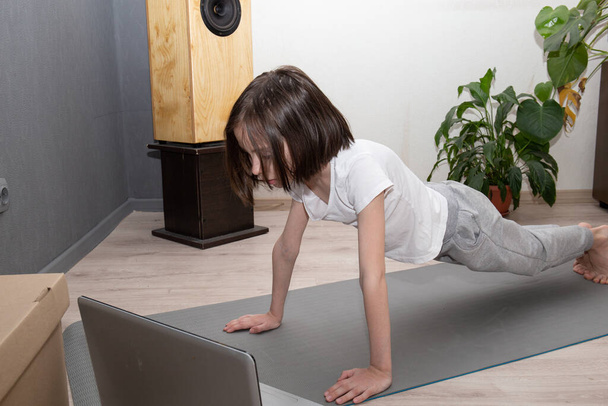 Дитячі дистанційні фізичні вправи вдома в її кімнаті. Дитина в дощатій позі
. - Фото, зображення