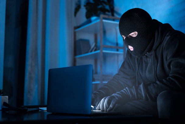 Masked hacker downloading private information using pc - Foto, Imagem