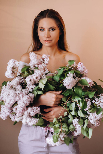 Beautiful girl with lilac flowers in her hands. A girl with lilac flowers in the spring at home. A girl with long hair and lilac in her hands. - Fotografie, Obrázek