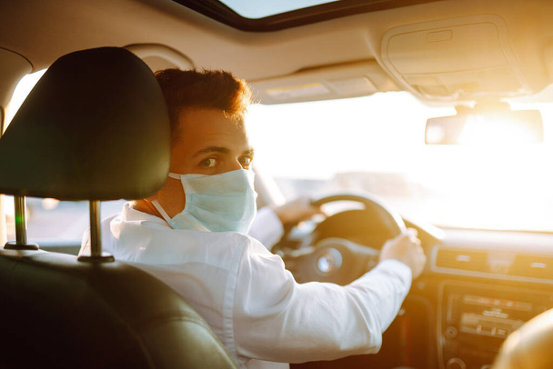 Man driving a car puts on a medical mask during an epidemic in quarantine city. Health protection, safety and pandemic concept. Covid- 19. - 写真・画像