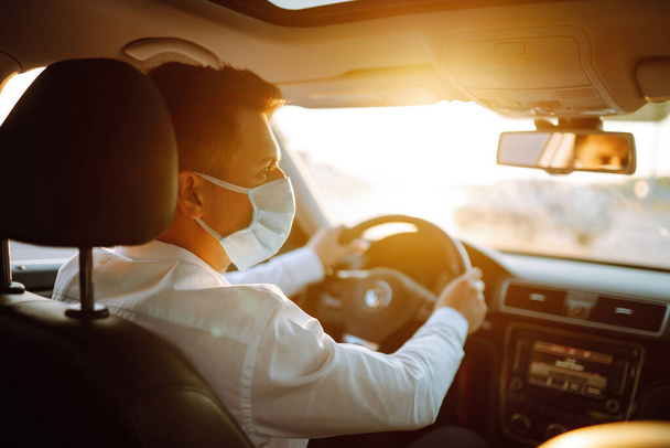 Man driving a car puts on a medical mask during an epidemic in quarantine city. Health protection, safety and pandemic concept. Covid- 19. - Zdjęcie, obraz