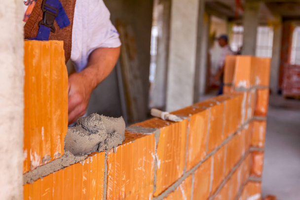 Mason, albañil trabajador está utilizando bloques rojos para montar una pared en el sitio de construcción
. - Foto, imagen