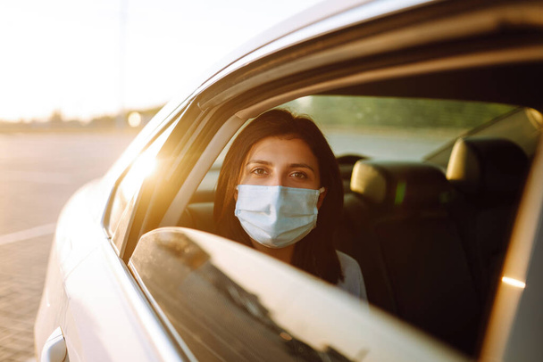Girl passenger in protective sterile medical mask in the taxi car during an epidemic in quarantine city. Health protection, safety and pandemic concept. Covid - 19.  - 写真・画像