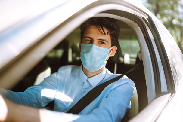 Young man  in protective sterile medical mask sits in the car during an epidemic in quarantine city. Health protection, safety and pandemic concept. Covid - 19. - Valokuva, kuva