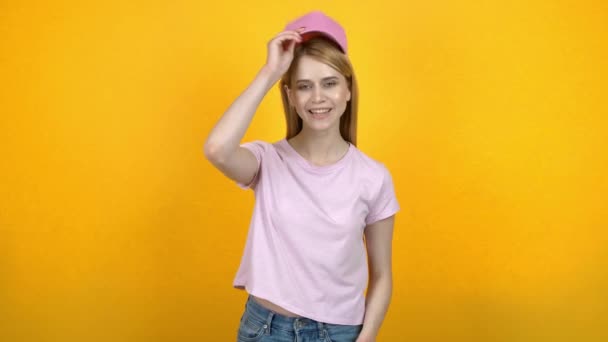 Young woman trying on different caps against color background - Πλάνα, βίντεο
