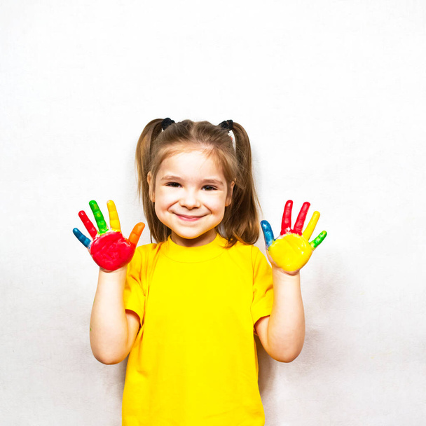 Beautiful little girl with hands in paint smiles in a yellow T-shirt. Childrens creativity. - Fotó, kép