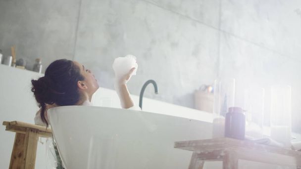Cerca de la mujer alegre que sopla espuma en el cuarto de baño ligero imn cámara lenta
. - Foto, Imagen