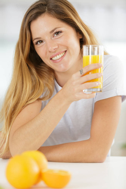 happy woman holding an orange juice looking at camera - Photo, Image
