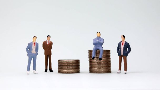 Bozuk para yığınının üzerinde oturan minyatür bir adam ve ayakta duran minyatür adamlar.. - Fotoğraf, Görsel