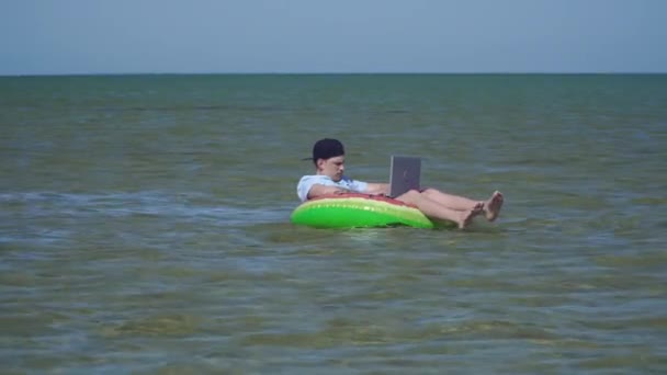 Un joven hombre de negocios está trabajando con entusiasmo detrás de un ordenador portátil balanceándose en las olas del mar
 - Metraje, vídeo
