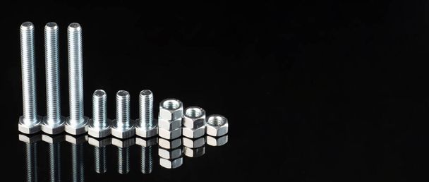shiny metal bolts and nuts of different sizes on a black mirror background - Foto, Imagem