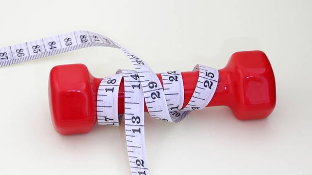 A red dumbbell and tape measure. - Photo, Image