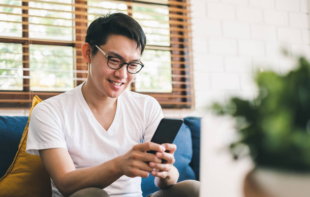 Giovane uomo asiatico utilizzando il telefono per lo shopping online, e lavorare con il computer portatile a casa - Foto, immagini