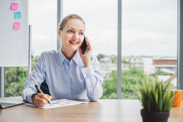 Jonge mooie zakenvrouw praten aan de telefoon en werken op tafel in een modern kantoor - Foto, afbeelding