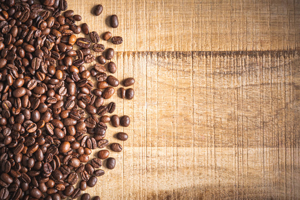 焙煎された茶色のコーヒー豆は木製のテーブルの背景にこぼれた。卓上ビュー - 写真・画像