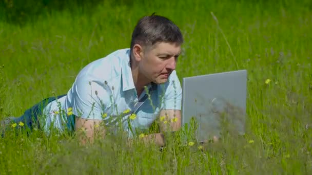 Podnikatel pracuje za laptopem ležícím na trávě - Záběry, video
