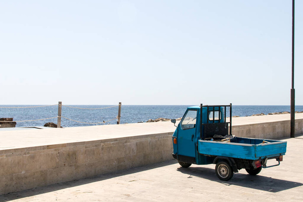 Kék tricikli a kikötőben, a tenger közelében. Jellemző szállítóeszközök és munkaeszközök - Fotó, kép