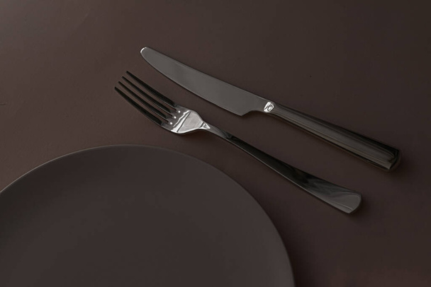 Empty plate and cutlery as mockup set on dark brown background, top tableware for chef table decor and menu branding - Photo, Image