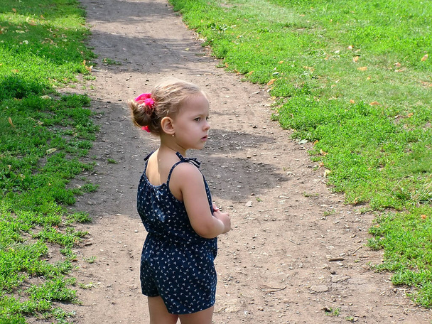 Маленька дівчинка на шляху в літньому парку. Озирнувся назад. Серйозний, сумний погляд
. - Фото, зображення