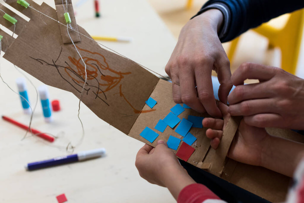 Діти носять роботизовану руку з картону. Дитяча прикраса картонної руки, зроблена під час майстерні STEAM. Наукові та робототехнічні заходи для дітей у школі. Навчання інкінгу та STEM
 - Фото, зображення