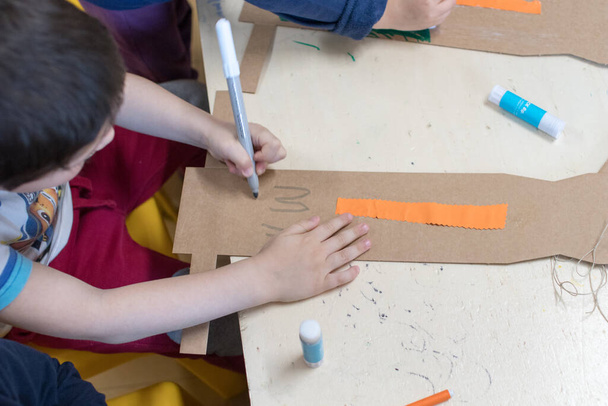 Children lleva un brazo robótico hecho con cartón. Decoración infantil de un brazo de cartón fabricado durante el taller STEAM. Actividades de ciencia y robótica para niños en la escuela. Tinkering y educación STEM
 - Foto, Imagen