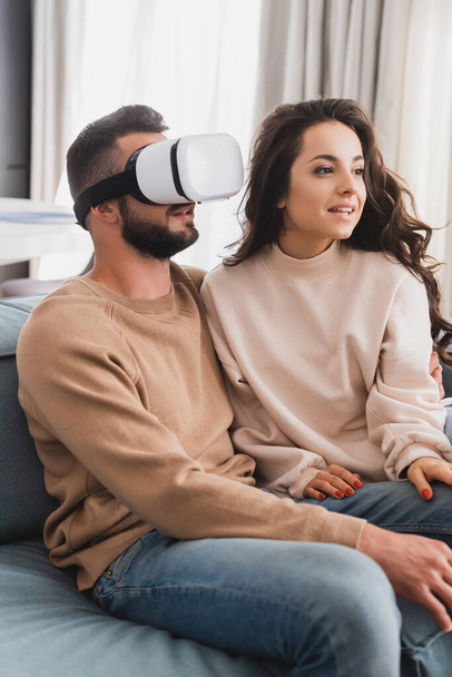 beautiful girl sitting on sofa near bearded boyfriend in virtual reality headset  - Fotó, kép