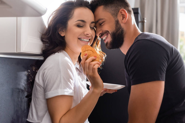 happy girl holding tasty croissant near cheerful man - Фото, зображення