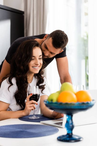selective focus of bearded man looking at happy girlfriend holding glass of red wine  - Foto, afbeelding