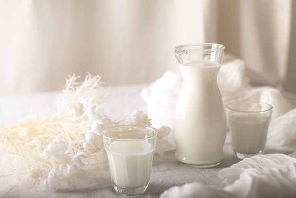 Milk in a jug and glasses on a white background. Table. Tablecloth. Flowers . copy space. - Foto, Imagen