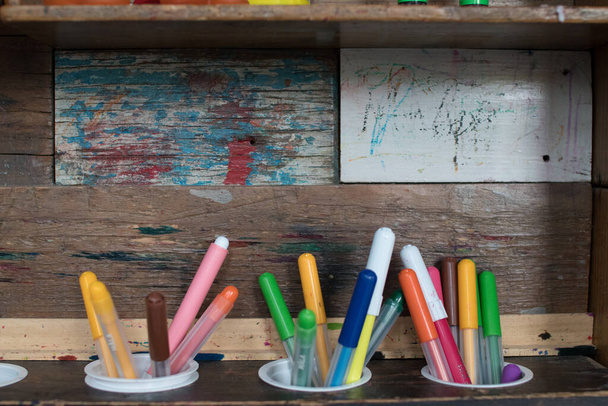 tres rotuladores con diferentes colores en un estante de madera con fondo rústico y colorido. herramientas para niños
 - Foto, Imagen