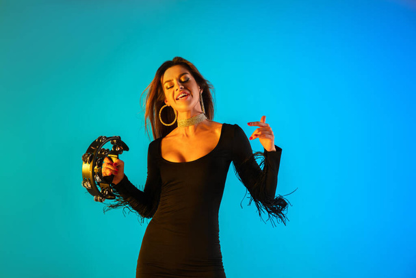 Caucasian female singer with tambourin isolated on blue studio background in neon light - Фото, зображення