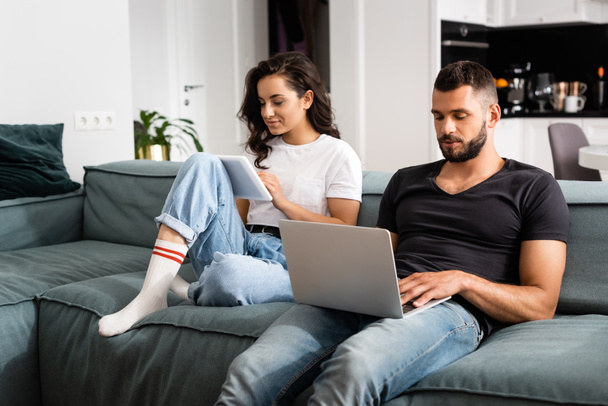 freelancer bonito usando laptop perto da namorada com tablet digital na sala de estar
  - Foto, Imagem