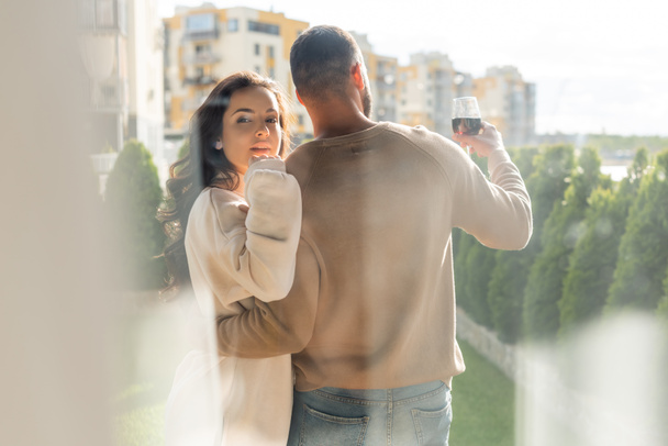 selective focus of man holding wine glass and hugging attractive girlfriend outside  - Фото, изображение