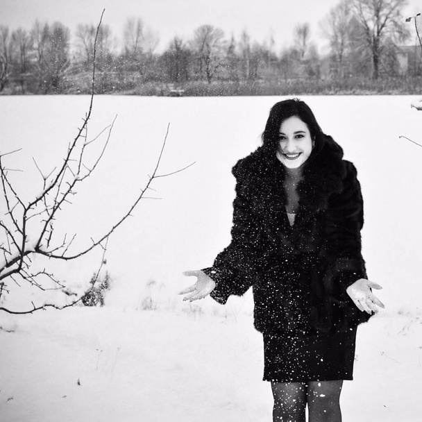 Plus size nice young lady in retro look style walk at winter time wear in not natural fur coat. Woman have a good mood. Winter holiday time, black and white photo - Foto, imagen