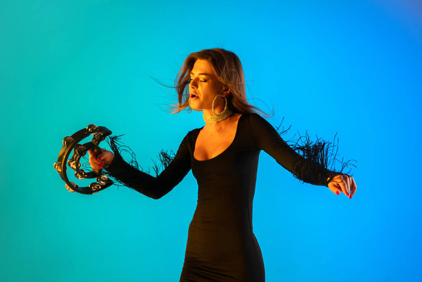Caucasian female singer with tambourin isolated on blue studio background in neon light - Foto, afbeelding