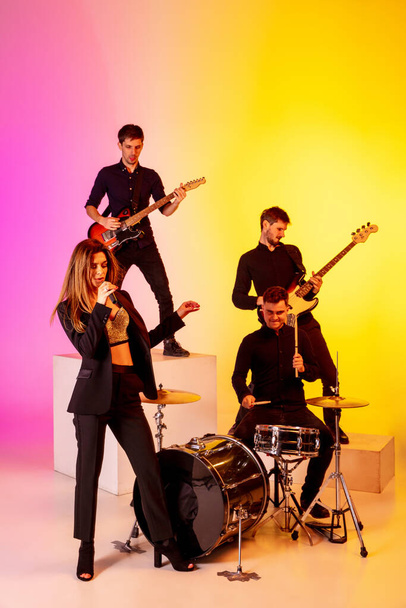 Young caucasian musicians, band performing in neon light on gradient studio background - Фото, зображення