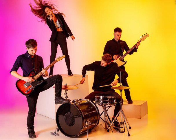 Young caucasian musicians, band performing in neon light on gradient studio background - Foto, Imagem